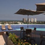 Cadeiras com sombrinha na mesa, piscina no terraço, vista para outros prédios